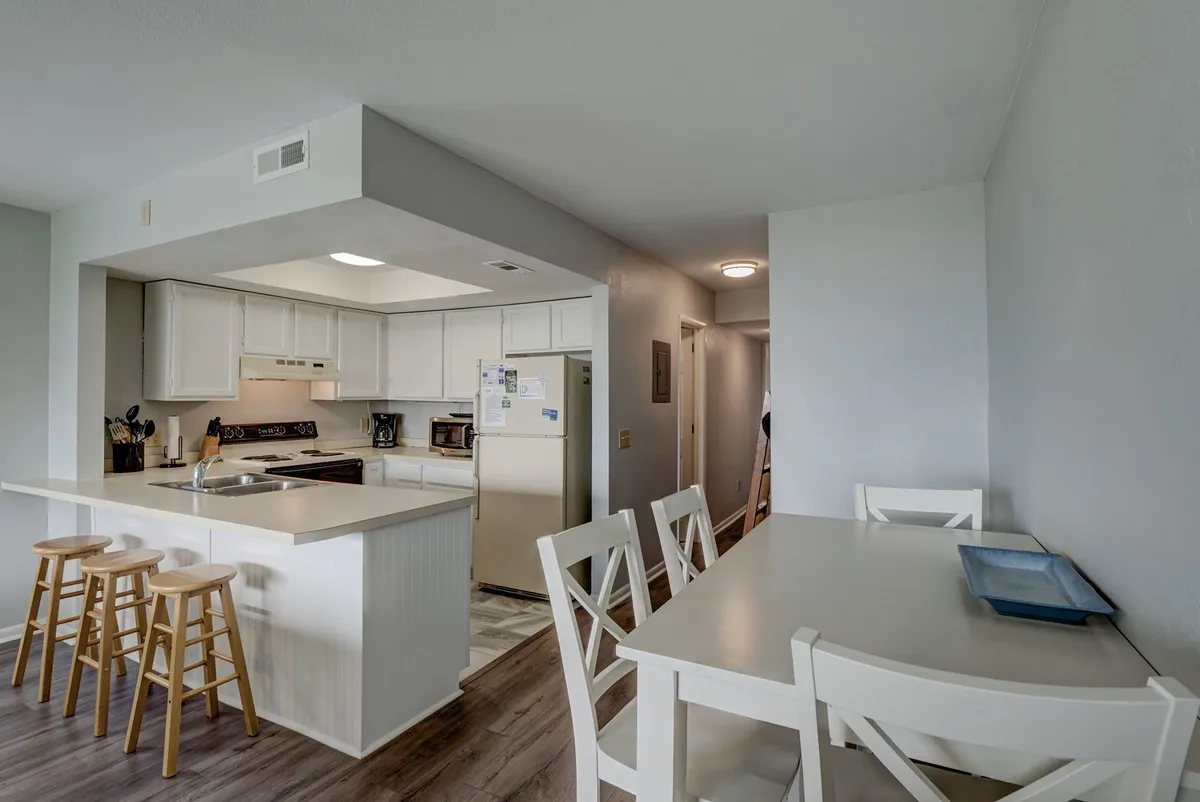 A casual, welcoming dining area includes a kitchen island, stools, and a dining table—arranged for both family meals and entertaining guests. Warm lighting and comfortable seating foster a sense of togetherness and celebration.