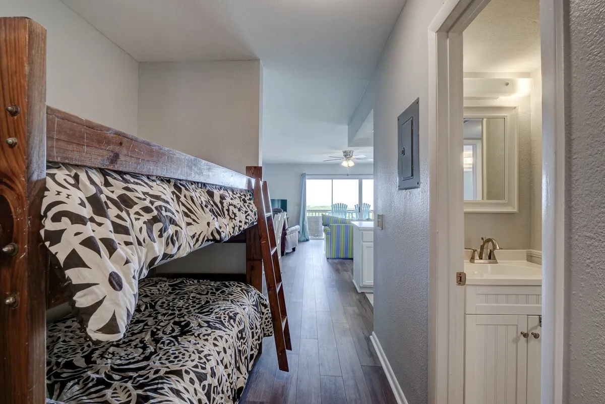 This interior shot highlights a playful bunk bed alcove within view of the main living space. The area is bright and family-friendly, with windows bringing in natural light and offering glimpses outside. The layout supports both playful afternoons for kids and shared family moments in the adjacent living area.