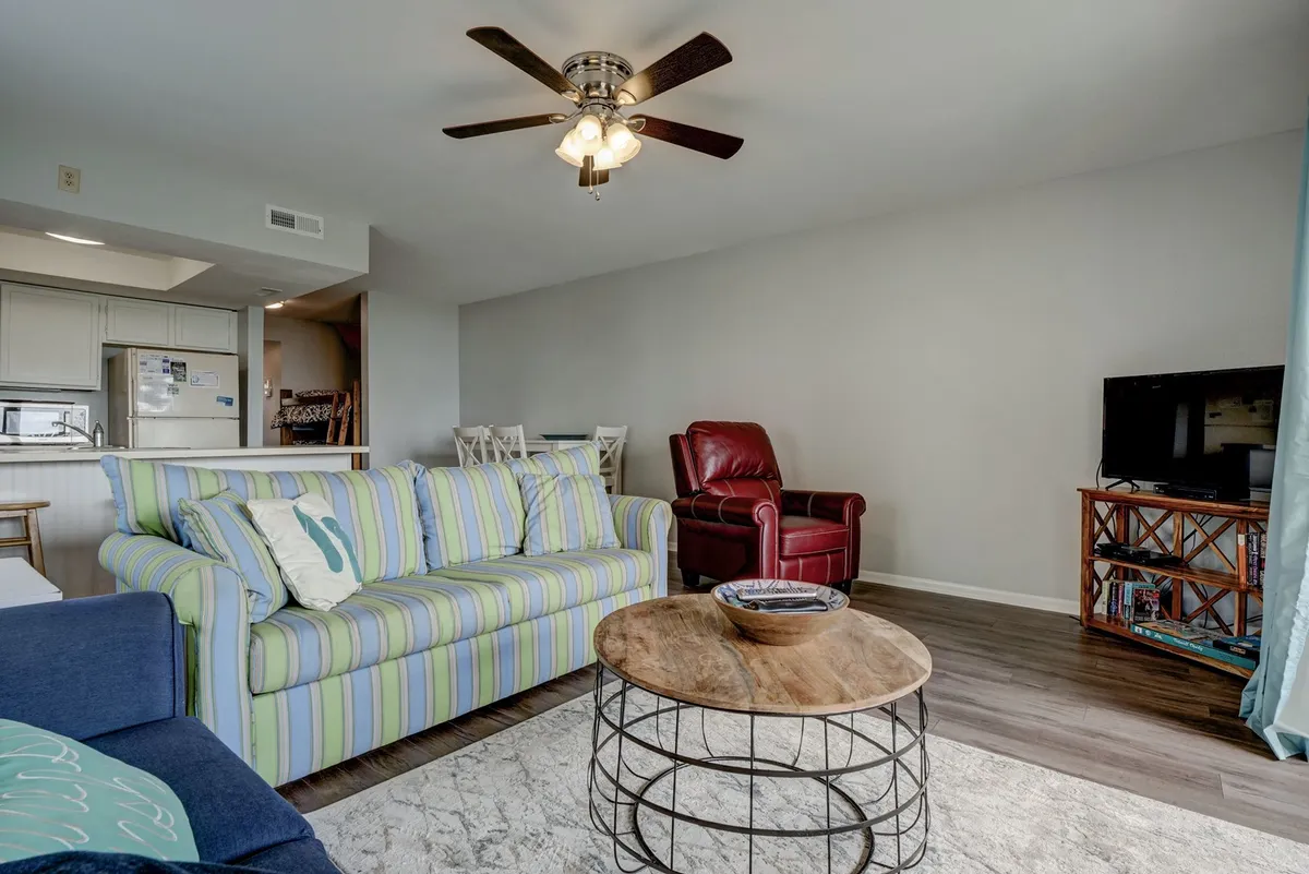 A comfortable, casual living area with a striped sofa, wooden coffee table, and red armchair arranged for socializing or relaxing after a day at the beach. The space feels inviting for groups and families, suggesting a homey environment for group meals or downtime together.