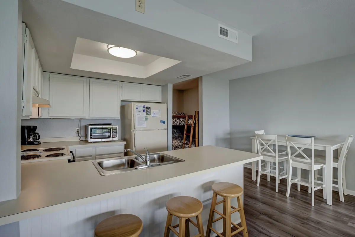 A welcoming, open-plan kitchen features a large island with stools, modern appliances, and a dining table set for a meal. The space is bathed in natural light, suggesting a lively, family-friendly environment perfect for gathering and sharing meals.
