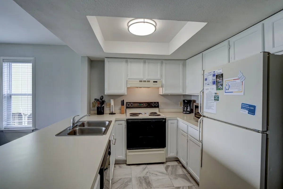 A homey kitchen is centered around an island, surrounded by updated appliances, a deep sink, and a window that brings in daylight. There are hints of both cooking and entertaining, with ample counter space for meal preparation and social interaction.