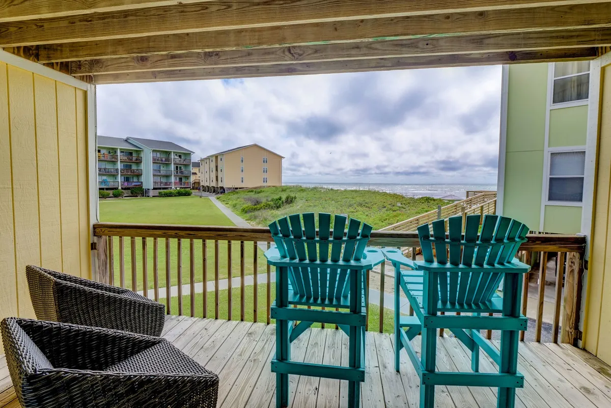 An exterior image featuring a serene seating area with turquoise and wicker chairs overlooking the sea. With nearby buildings visible in the background, the scene offers a sense of both privacy and community. It’s a tranquil spot to watch the sunset, enjoy dolphin sightings, or simply unwind together.