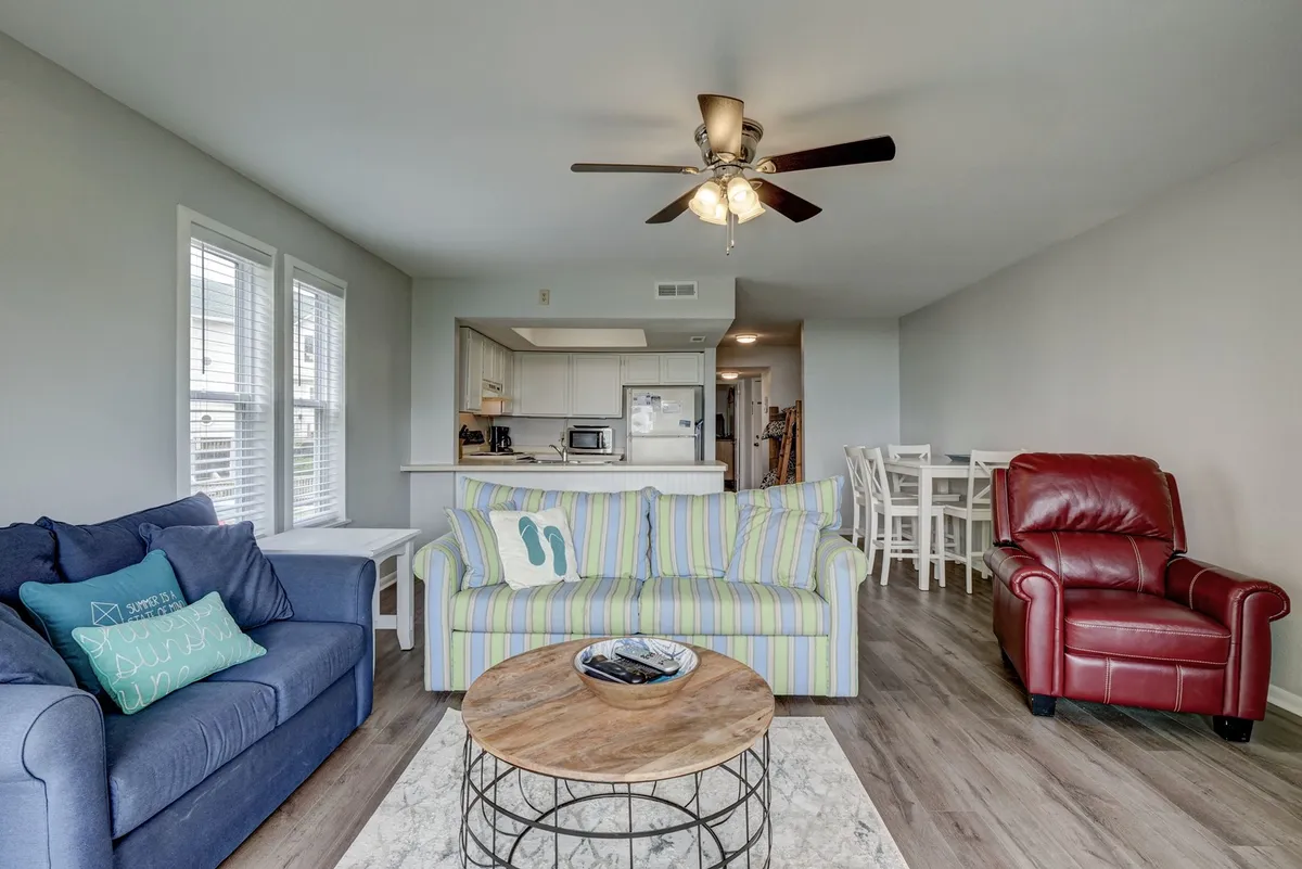 A welcoming living area featuring a striped sofa that can double as a pull-out bed, a wooden coffee table, and a red recliner. The dining area is visible in the background, emphasizing the spaciousness and multifunctionality of the room.