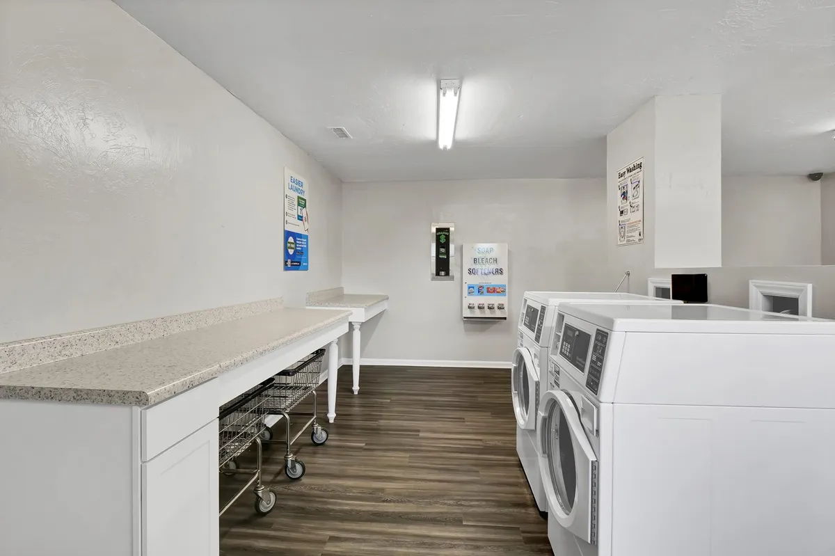 This image displays a practical onsite laundry room featuring washing machines, dryers, and a large folding countertop. The space is clean, bright, and organized, ideal for travelers looking to complete chores efficiently without leaving the property.